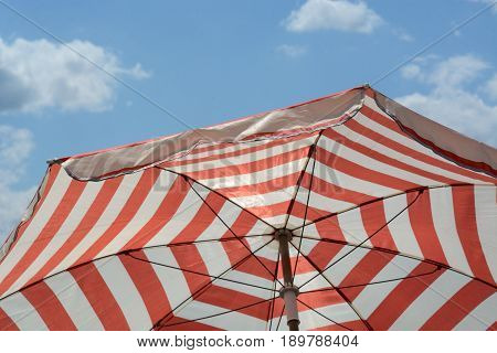 Red striped umbrella parasol to provide shade and sun protection against blue sky with light clouds