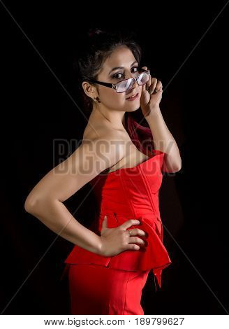 Pretty young sexy asian model with red hair and glasses in amazing red dress on dark background.