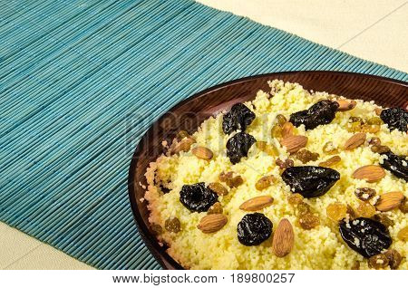 Plate with freshly cooked Moroccan couscous with almond and prunes on blue straw background