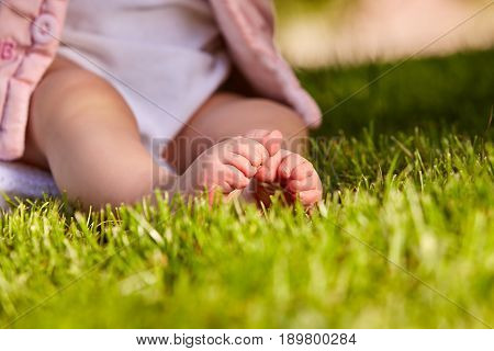 Small baby feet on the green grass at summer sunshiny day in the park. Cute baby in the white clothing. Horizontal croped photo. Concept of the happy babies.