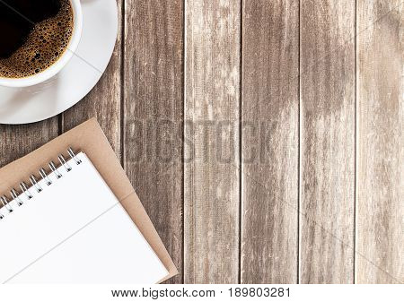 Top view cup of coffee and notebook on wooden table with copy space