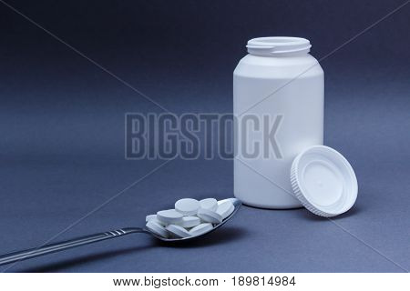 White round pills medicine in steel spoon and white bottle with its lid behind