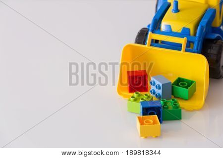 Closeup of children toy tractor with colorful plastic bricks or details on white background. Baby's toys on the table isolated.