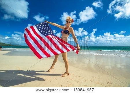 Smiling woman with american flag bikini waving american flag in spectacular tropical Lanikai Beach, east shore of Oahu in Hawaii, USA. Enjoying and freedom in Hawaiian vacations. Patriotic concept.
