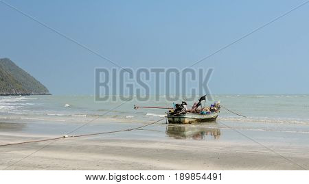 Small woodenl fishing boat (Longtail boat) anchored on beach at low tide in Thailand