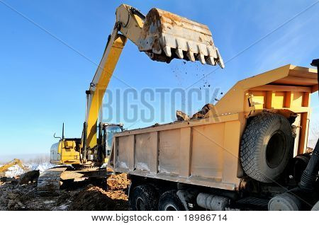 Loader Excavator loading body of a dump truck tipper at open cast over blue sky in winter	