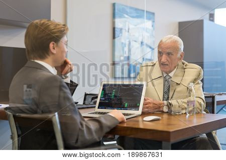 Young financial advisor sitting in front of laptop, consulting senior client with his investment strategy.