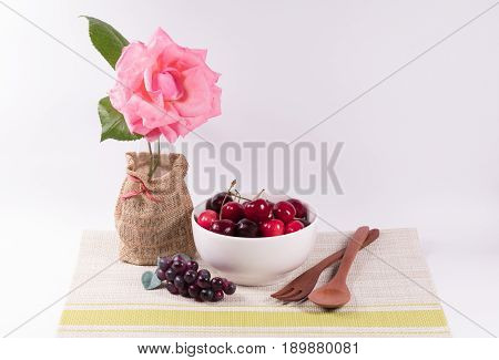 Cherries in white bowl and wooden spoonflower on white background