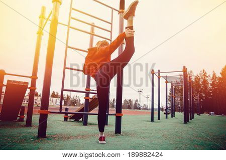 Girl on the sports field stretches the muscles of the legs and back, vertical twine. Concept of a healthy lifestyle and exercises to strengthen the hands and back and joints.