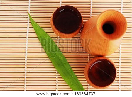 SAKE liqueur in a brown wooden bottle on a light brown background.