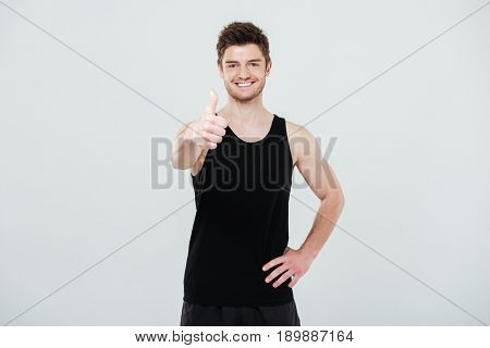 Image of happy young sportsman standing isolated over white background. Looking at camera showing thumbs up gesture.