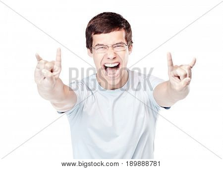 Young excited hispanic man wearing glasses and blue t-shirt, showing horns hand gesture with both hands and happy screaming isolated on white background - joy concept