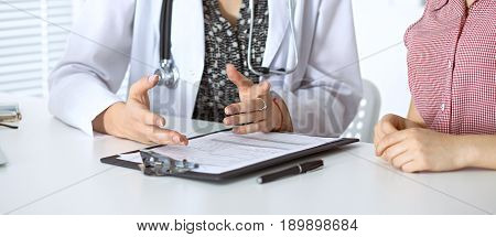 Doctor and patient sitting at the desk. Physician pointing into medical history records and explaining something to young woman. Medicine and health care concept.