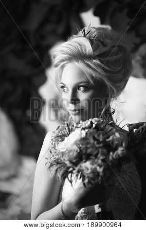 Beautiful blonde bride with blue eyes voluminous hairdress holding a bouquet smiling and looking away black and white frame