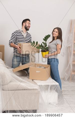Man and woman moving in new home. Happy couple unpacking boxes in living room witn new furniture covered with foil.