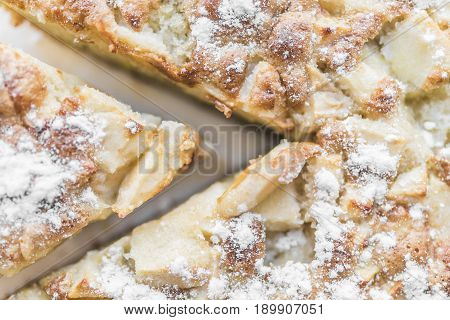 Apple pie and a cut piece of pie are sprinkled with powdered sugar and lie on a white plate close-up view