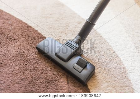 A vacuum cleaner with a black brush cleans the carpet with a dark and light brown pattern.