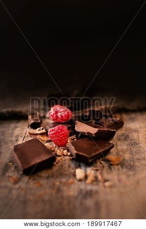 Broken chocolate bar with red ripe raspberries on dark brown background close up macro