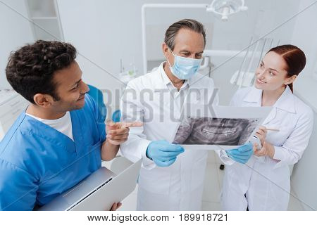 Make decision. Serious dentist wearing mask looking straight at picture while explaining the meaning to his interns