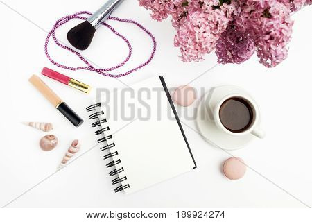 Spring lilac flowers on workdesk female home office with note and coffee white background top view