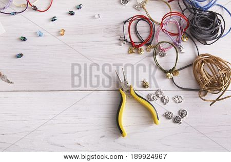 Handmade bracelets making, artisan workplace background. Top view on table with braid, pendants and accessories with pliers, copy space