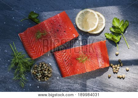 Two pieces of raw wild salmon fish steaks with lemon, capers and herbs, ready to cook, from above.