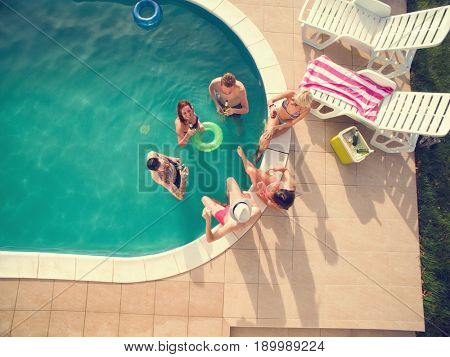 Group of young people in swimming pool drinking cold bear at summer