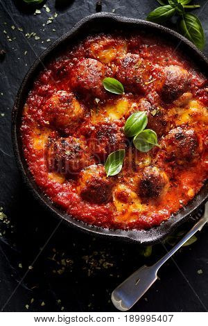Meatballs in tomato sauce with addition cheese and fresh basil on iron pan, black background, top view
