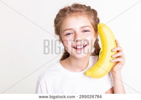 Laughing Light-haired Young Girl Holding Plastic Banana Near Her Ear