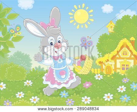 Friendly Smiling Easter Bunny With A Basket Of Colored Eggs Walking In Front Of A Small Hut Among Fl