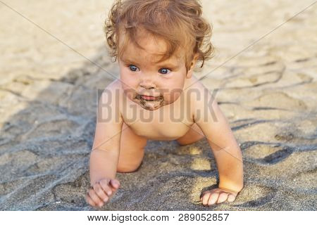 Baby girl crawling in the sand on the beach. Del Duque beach, Tenerife island, Canary.