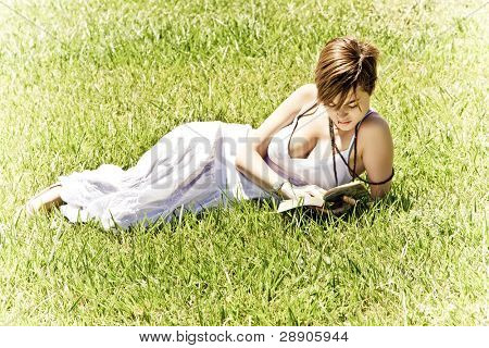 美しいブロンドの女性は草の上を読んでします。