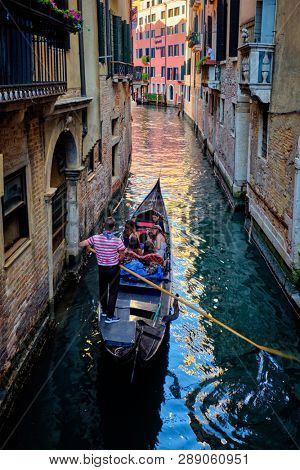 VENICE, ITALY - JUNE 27, 2018:  Narrow canal between colorful old houses with gondola boat with tourists and gonolier in Venice, Italy