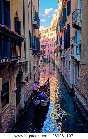 VENICE, ITALY - JUNE 27, 2018:  Narrow canal between colorful old houses with gondola boat with tourists and gonolier in Venice, Italy