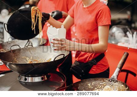 Chef Putting Noodles In Carton Box To Go From Pan On Fire At Open Kitchen. Fried Chinese Japanese No