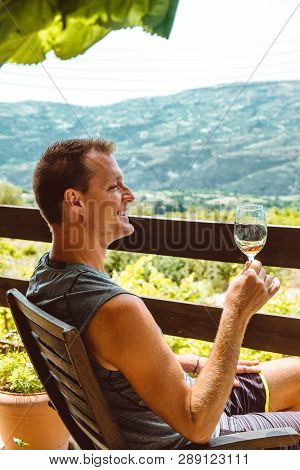 A Handsome Adult Man Sits On A Farm And Tastes A Glass Of White Wine. Sunny Day, Cyprus.