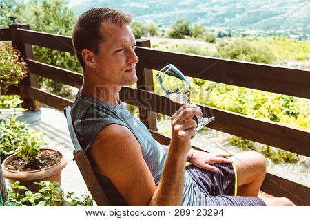 A Handsome Adult Man Sits On A Farm And Tastes A Glass Of White Wine. Sunny Day, Cyprus.