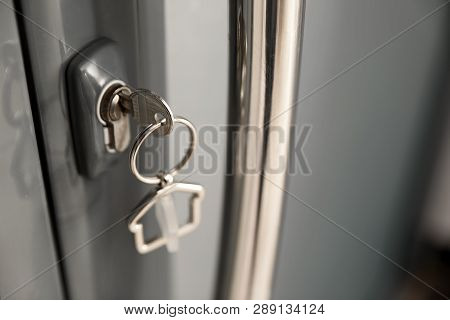 Key With House-shaped Trinket In Door Lock, Closeup. Space For Text