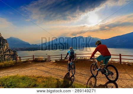 Cycling woman and man riding on bikes at sunrise mountains and Garda lake landscape. Couple cycling MTB enduro flow sentiero ponale trail track. Outdoor sport activity.