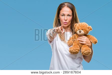 Middle age hispanic woman holding cute teddy bear plush over isolated background pointing with finger to the camera and to you, hand sign, positive and confident gesture from the front