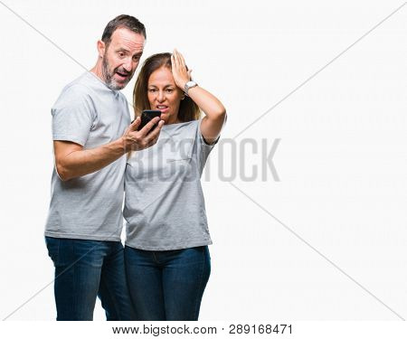 Middle age hispanic couple texting message on smartphone ver isolated background stressed with hand on head, shocked with shame and surprise face, angry and frustrated. Fear and upset for mistake.