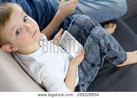 Boy Sitting, Looking At The Camera And Using Mobile Smart Phone At Home. Сhild Hands With A Smartpho