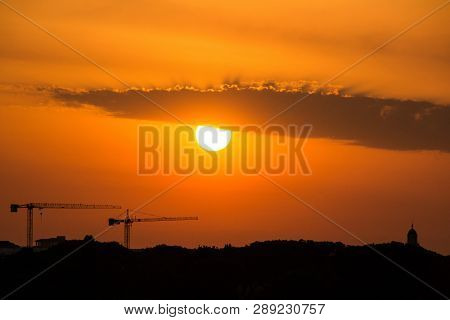 Silhouettes Of Two Construction Cranes And The Dome Of Church On The Background Of The Amazing Eveni