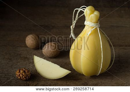 Head And Slice Of Typical Italian Cheese Caciocavallo With Walnuts On A Wooden Surface.