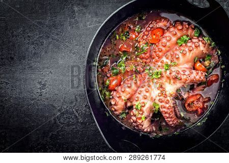 Traditional Greek octopus braised cooked with tomatoes and herbs in ouzo sauce as top view in a cast-iron saucepan with copy space left