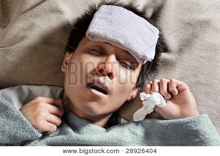Um doente dormindo masculino com molhar a toalha na testa para reduzir a febre alta alta