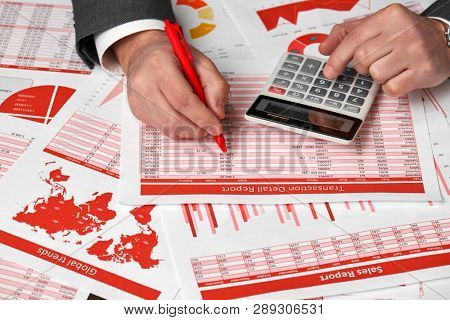 Businessman accountant using calculator for calculating finance on desk office. Business financial accounting concept Red reports and graphs. Office employee examines schedules and reports.