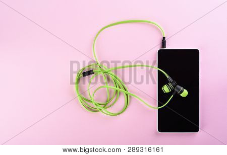Green Earphones Connected To A Smartphone Isolated On A Pink Background. Accessories For Individual 