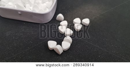 Close Up Of Several Small White Candy On Black Background Near Open Metal Box Filled With Mint Candy