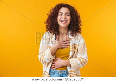 Image of pleased woman 20s with curly hair standing and laughing, isolated over yellow background